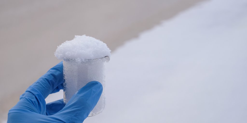 Bilde av en hånd med blå hanske som holder snø i en beholder 