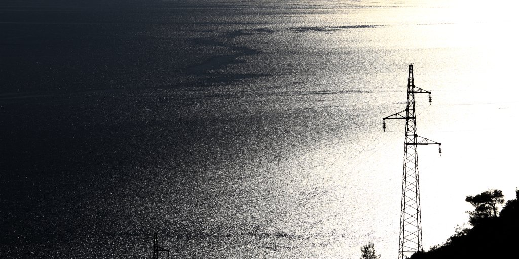 Electricity pylon with many cables on blue and yellow sea