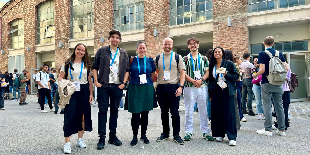 Seks mennesker med navneskilt rundt halsen står foran en murbygning i Wien.