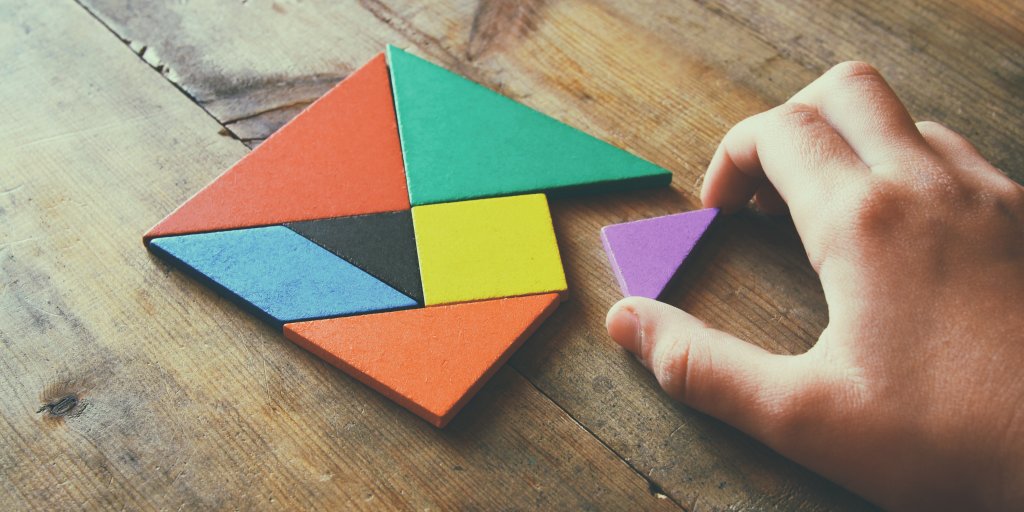 kid's hand holding a missing piece in a square tangram puzzle, over wooden table. 