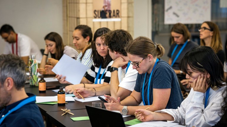 Flere mennesker sitter og jobber sammen på et avlangt bord inne i et klasserom.