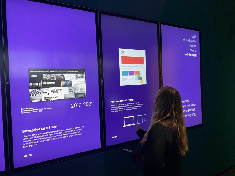 En designer står foran en stor touchskjerm og trykker på forskellige enheter for å se hvordan en nettside kan endre størrelse.