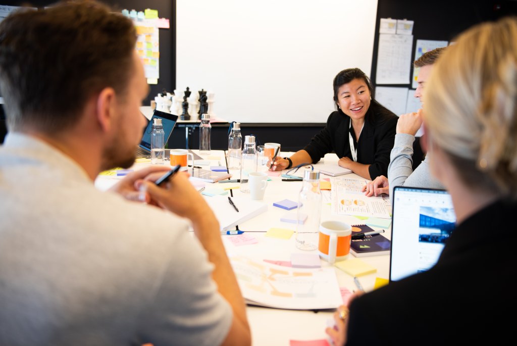 På bildet ser vi flere personer sitte rundt et bord og diskutere