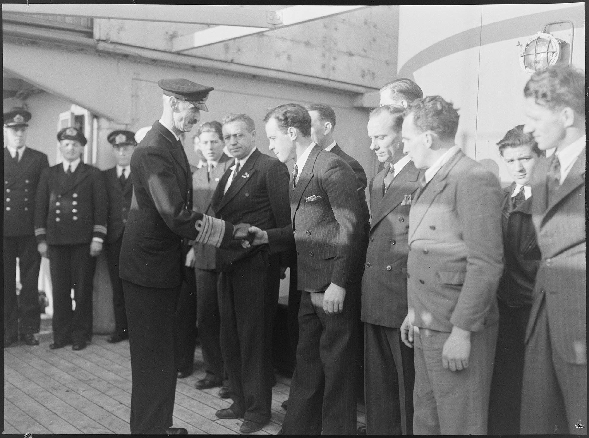 I juledagene 1944 avla H.M. Kong Haakon ledsaget av direktør Hysing-Olsen et besøk ombord på den norske handelsbåten "Sophocles". Kongen hilser på skipsmannskapet.  London, 15.1.1945. (Original bildetekst)